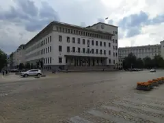 Сградата на Българската народна банка в София с часовниковата кула, павиран площад, саксии с цветя и паркирани коли