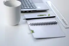 Лаптоп, тетрадка, линийка и чаша върху бяло работно бюро
